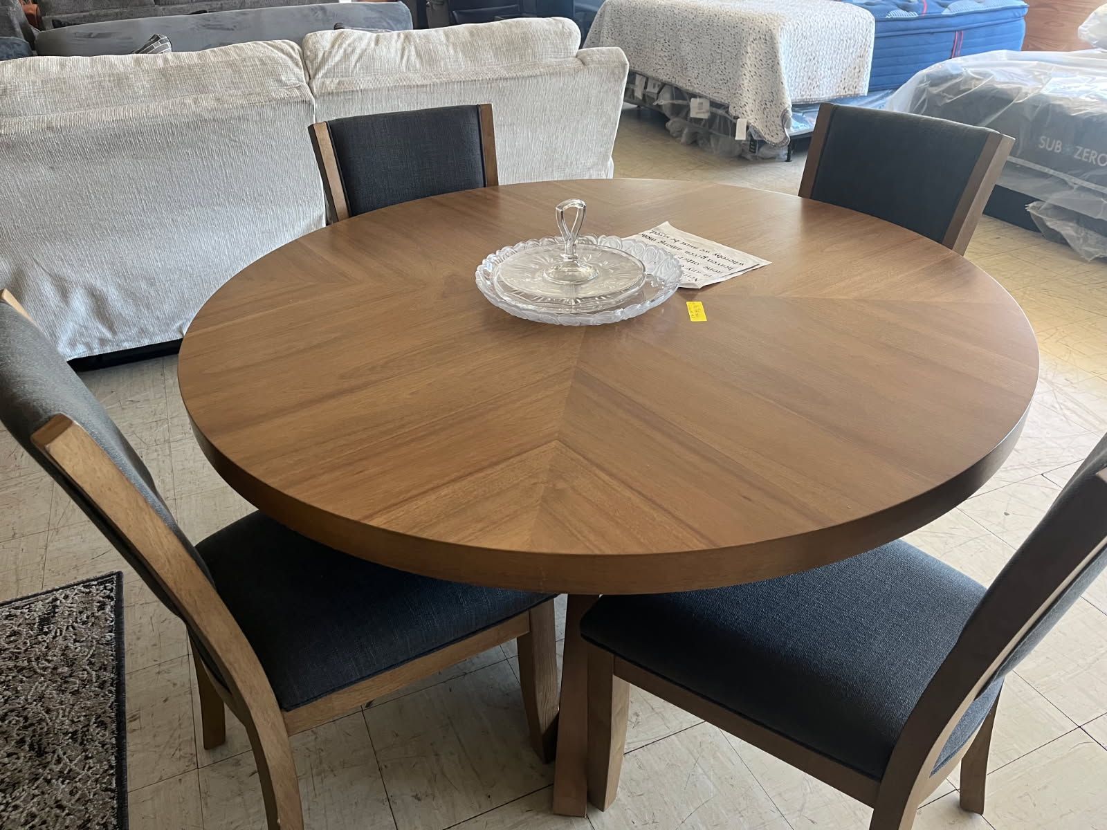 Round wooden dining table with four dark chairs and a decorative tray in a bright living room.