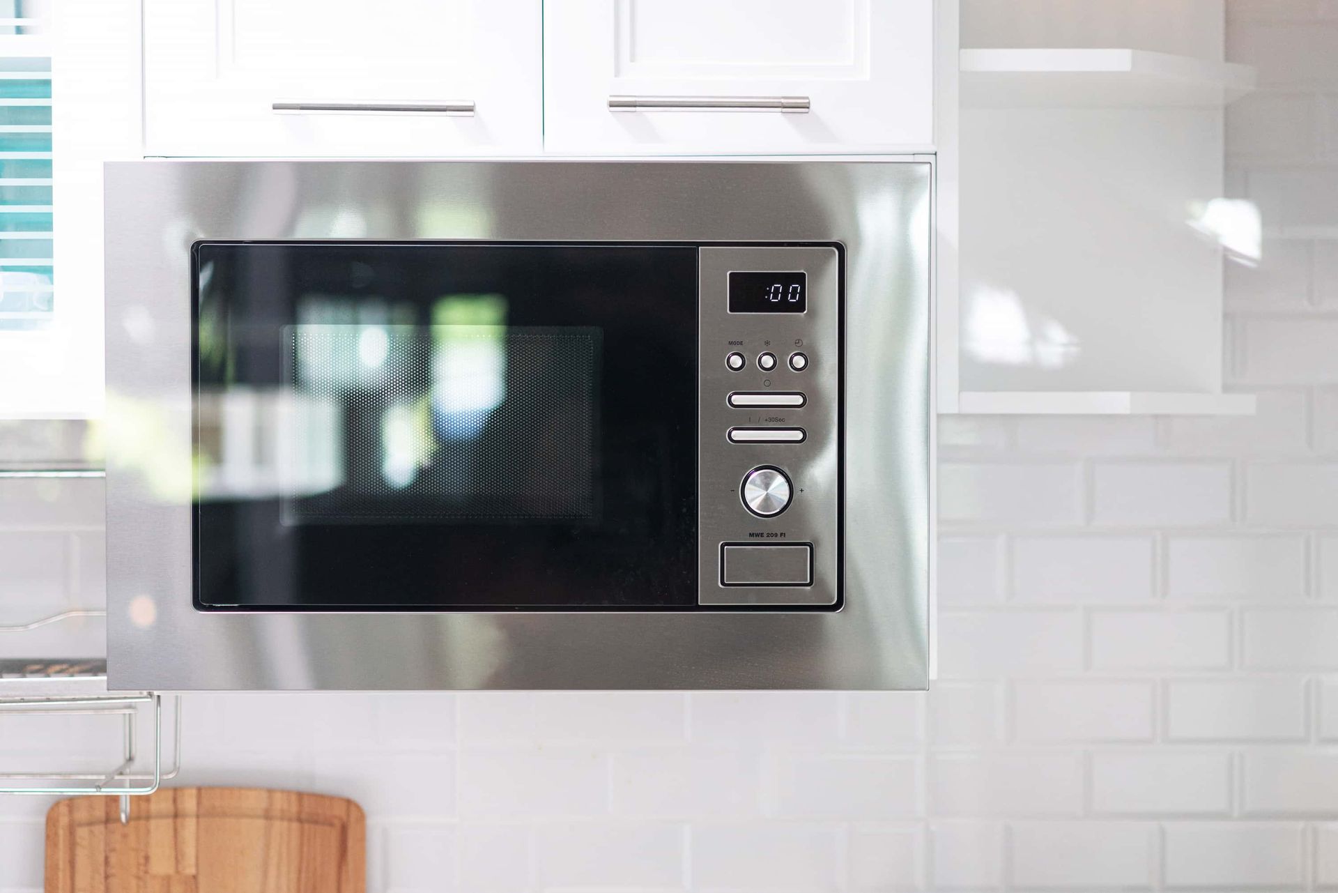 Stainless steel microwave built into white kitchen cabinets, with a black window and digital control panel