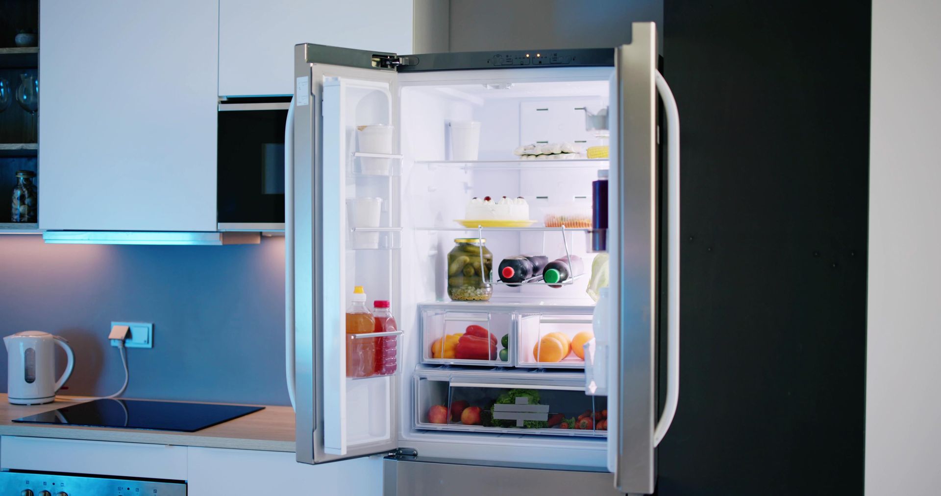 Open refrigerator in a modern kitchen with shelves of fruit, drinks, and condiments.