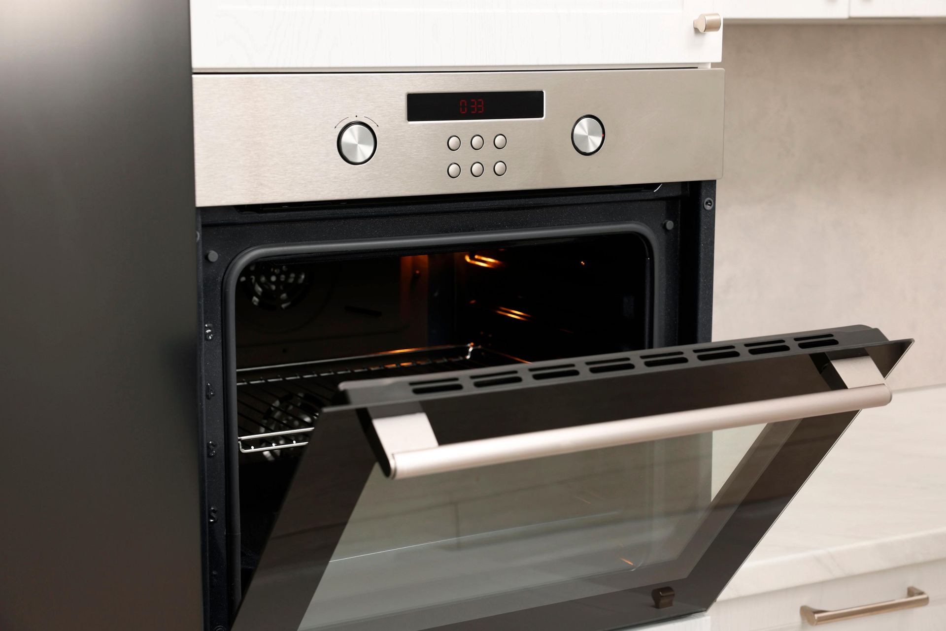 Open oven door in a modern kitchen, showing the lit interior and stainless steel control panel.