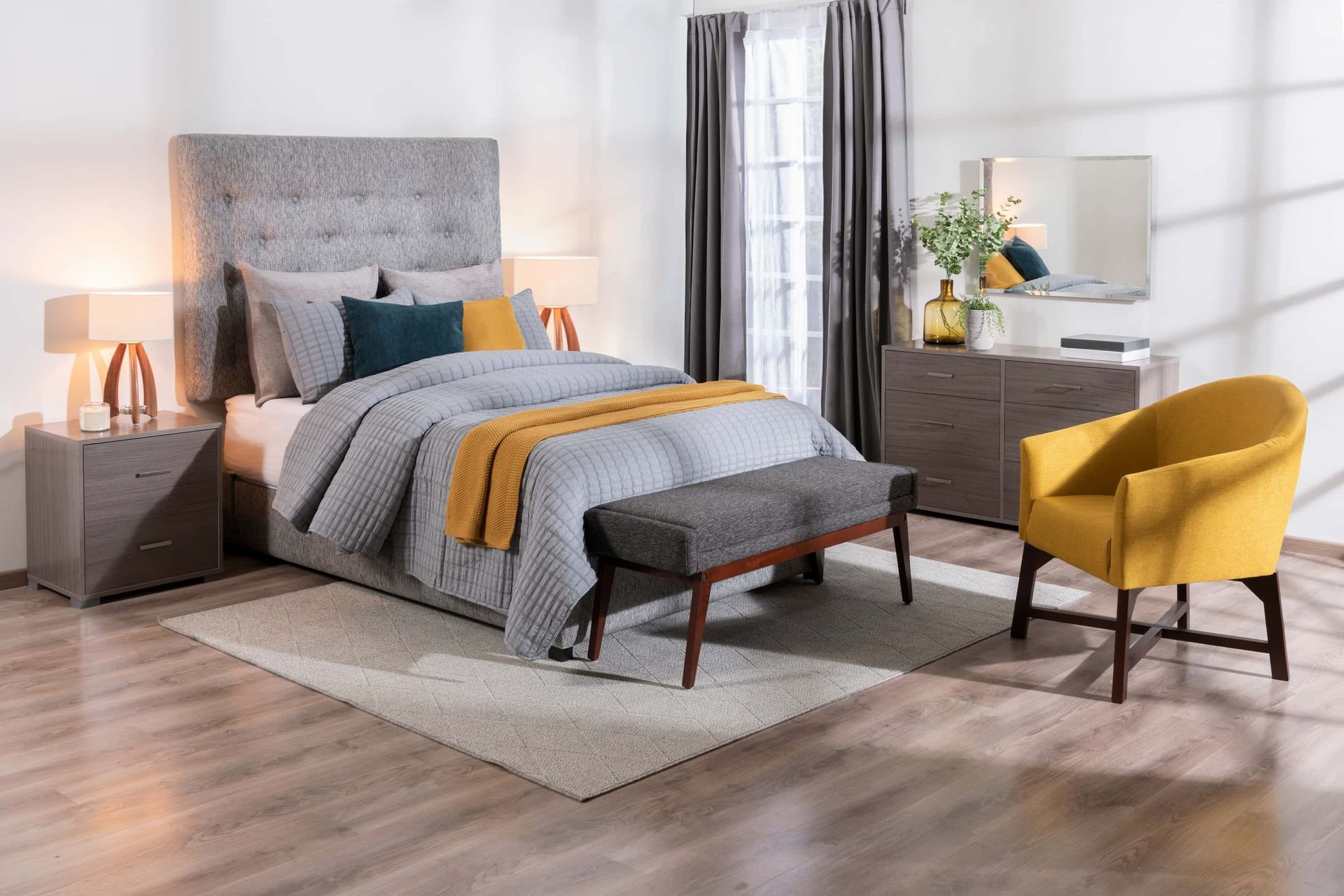Modern bedroom with gray bed, yellow throw, bedside lamps, dresser, mirror, and yellow chair