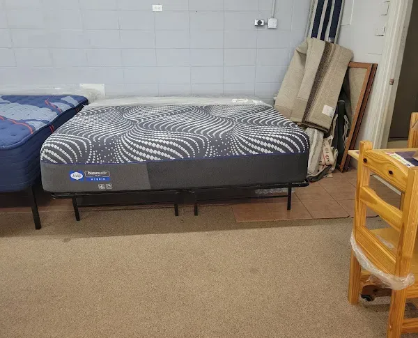 Small room with two single beds, a patterned mattress, and stacked boards leaning against a wall.