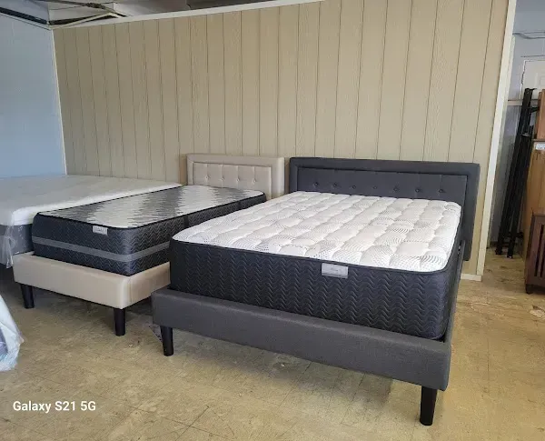 Two upholstered mattresses on display in a showroom, one dark gray and one light gray with white quilting.