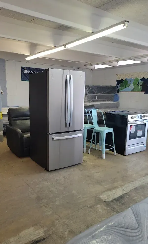 Basement room with stainless steel refrigerator, black sofa, blue chair, and an electric stove.