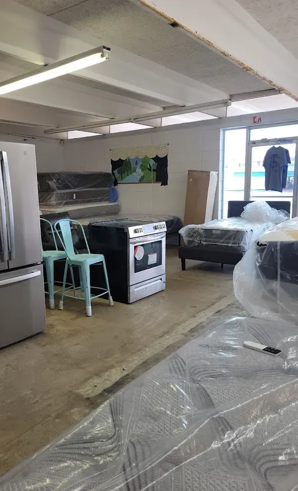 Storage area with stove, refrigerator, covered furniture, and stacked chairs in a basement-like room