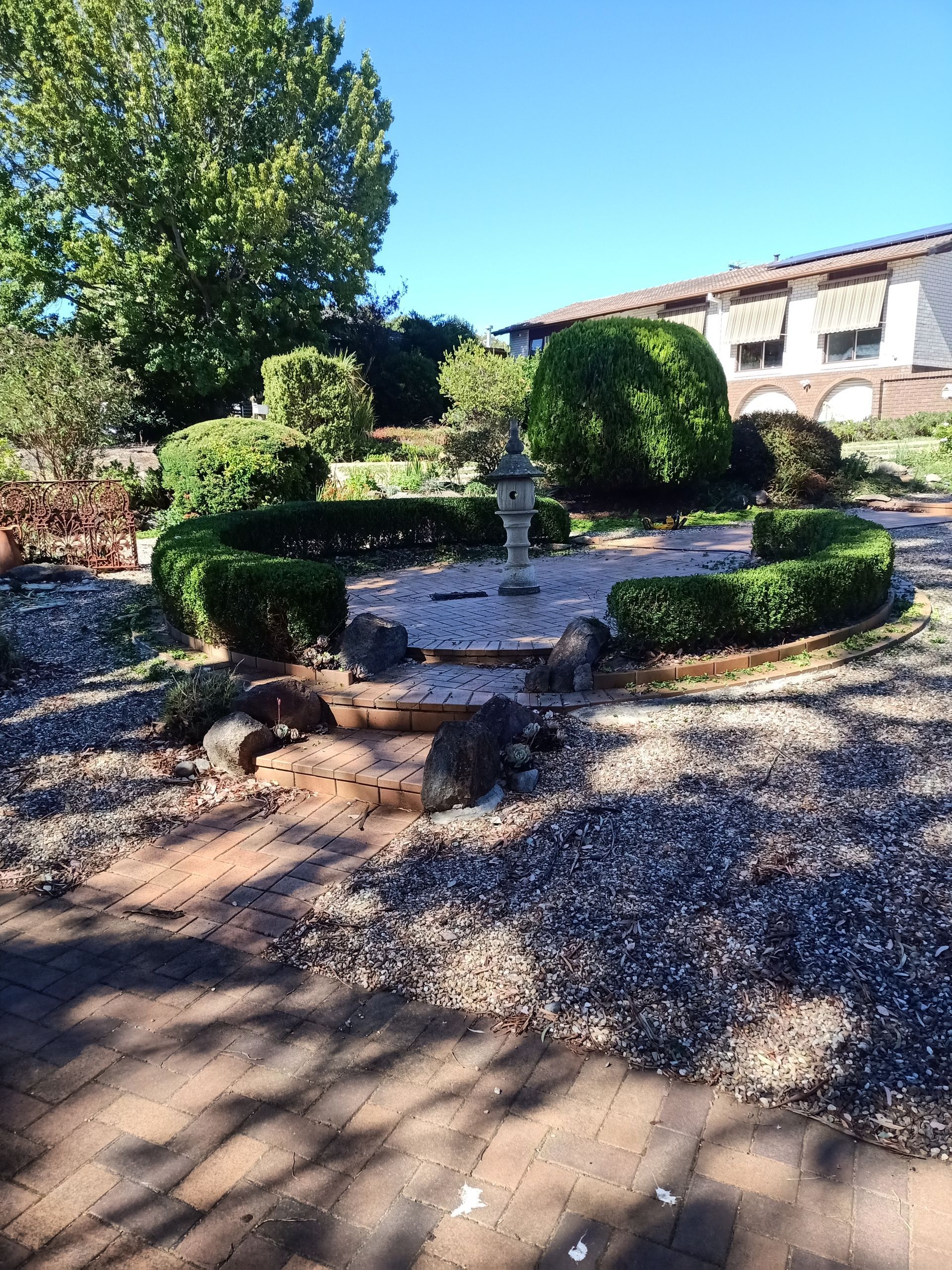 Stone fountain surrounded by trimmed hedges in a garden setting, sunlight casting shadows. — Your Garden in Charnwood, ACT