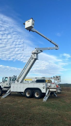 A bucket truck is parked in a field with a blue sky in the background.