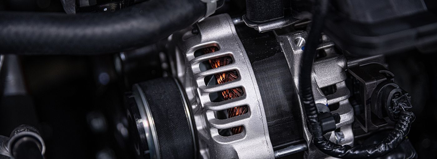 Close-up of a car alternator. Silver housing with copper-colored interior; black hoses and parts surround it.