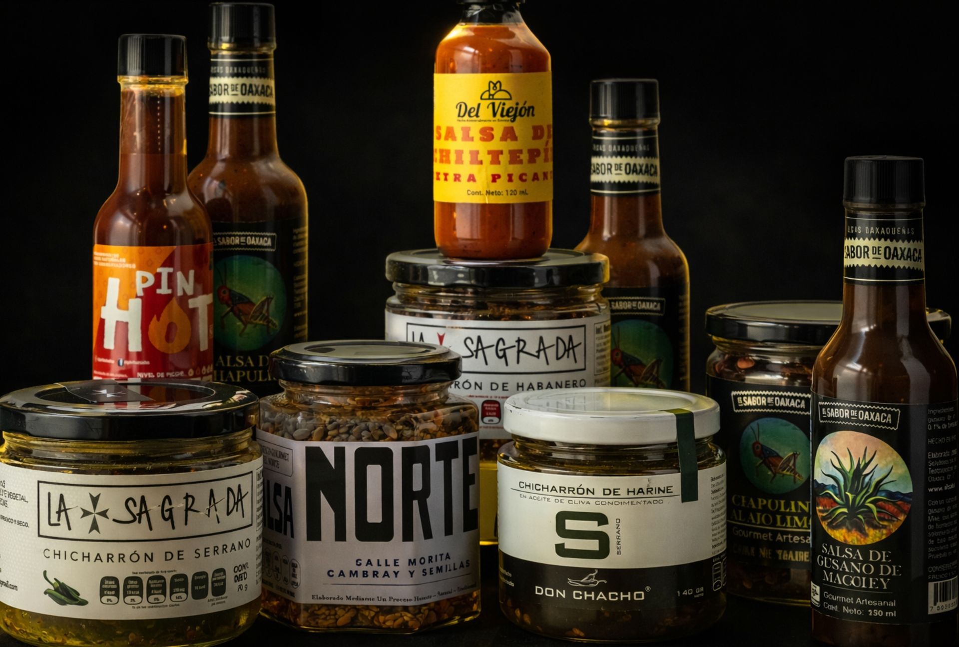 Assorted hot sauce bottles and jars arranged on a dark surface against a black background.