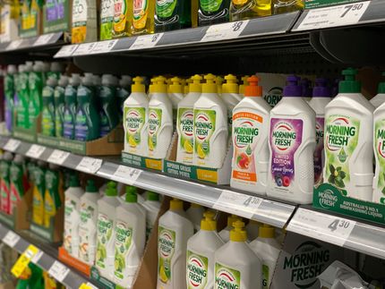 A grocery shelf lined with assorted colorful cleaning bottles and spray cleaners.