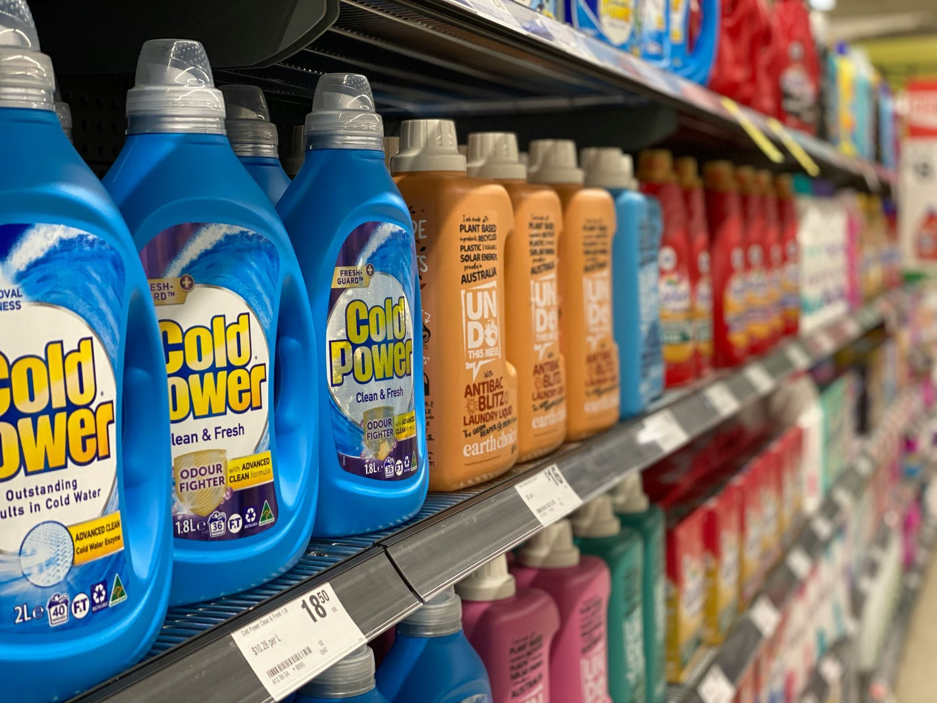 A grocery store shelf lined with colorful laundry detergent bottles, including blue and orange bottles.