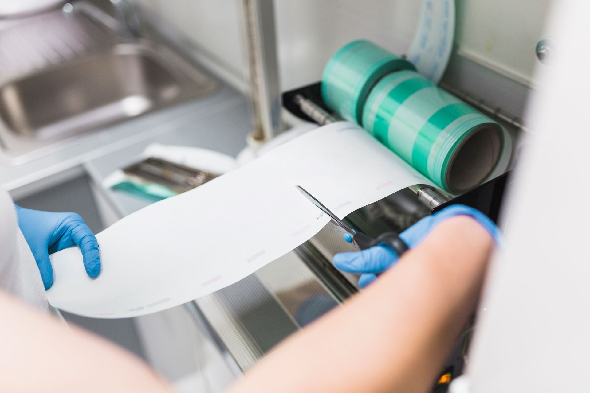 Hands cutting white material with scissors in a workshop, beside a green-striped roll on a machine