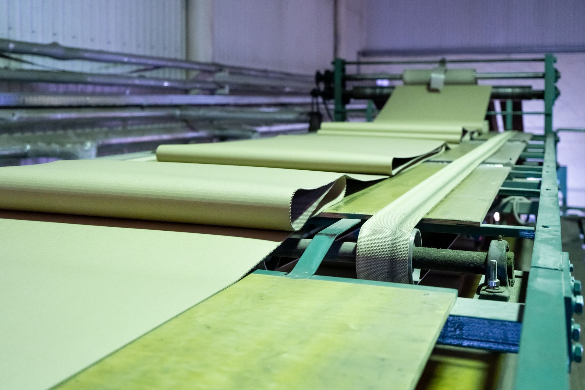 Large rolls of beige material moving along an industrial conveyor in a factory.
