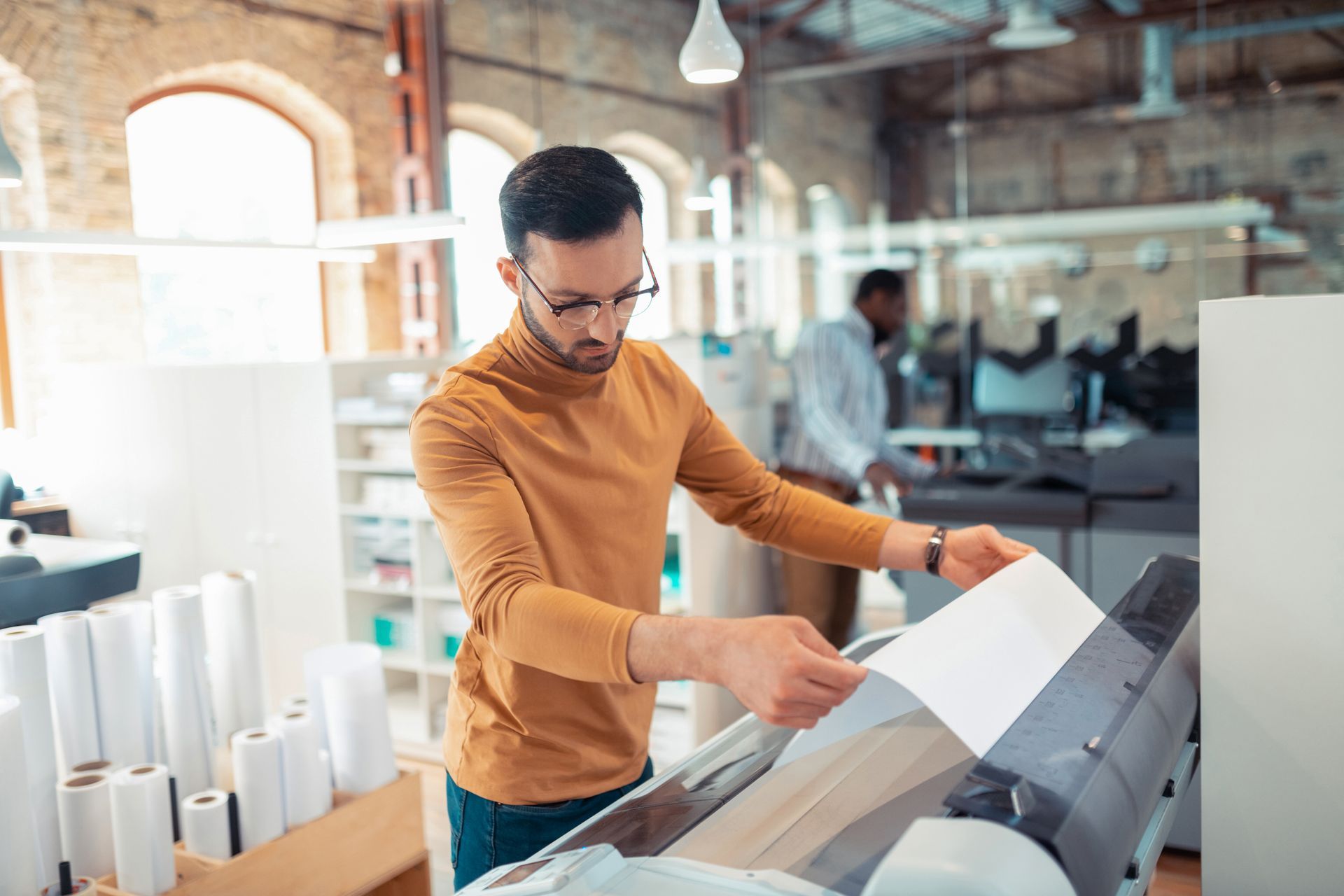 Man in orange sweater examining a large print in a bright design studio