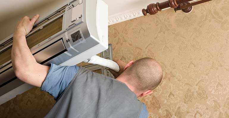 An image showing a professional technician installing a ductless mini split system in a room.