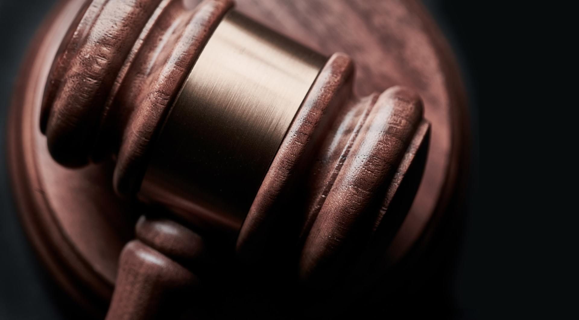 A close-up of a wooden judge's gavel resting on a matching wooden sounding block against a dark background.