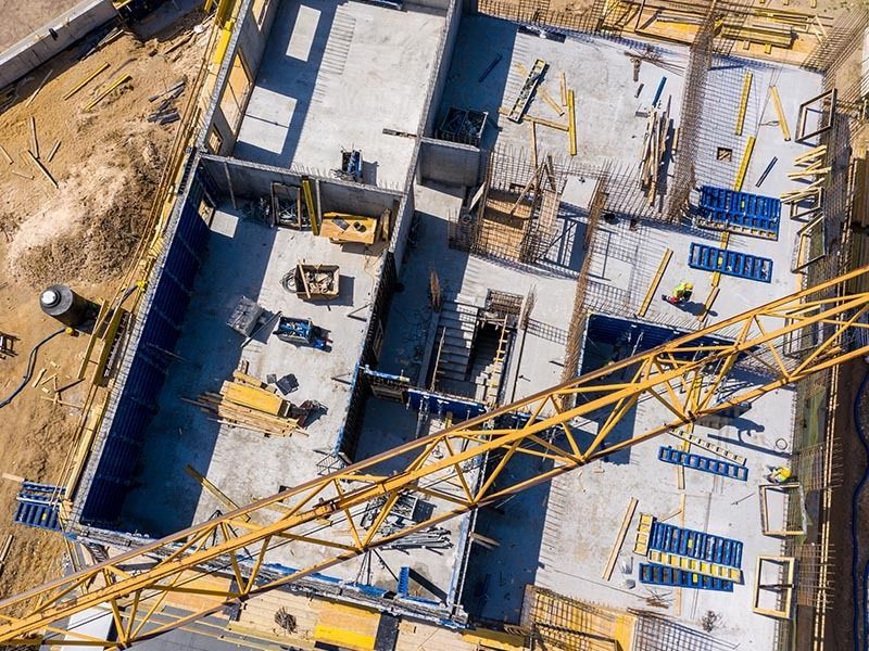 An overhead drone shot of a building construction site featuring concrete floors, wall forms, and a large yellow crane.