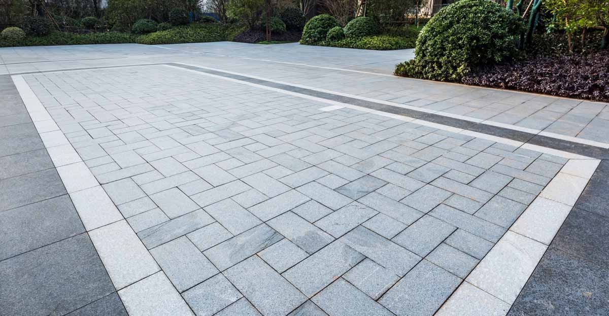A driveway paved with rectangular light grey stones in a herringbone pattern, bordered by white and dark grey pavers.