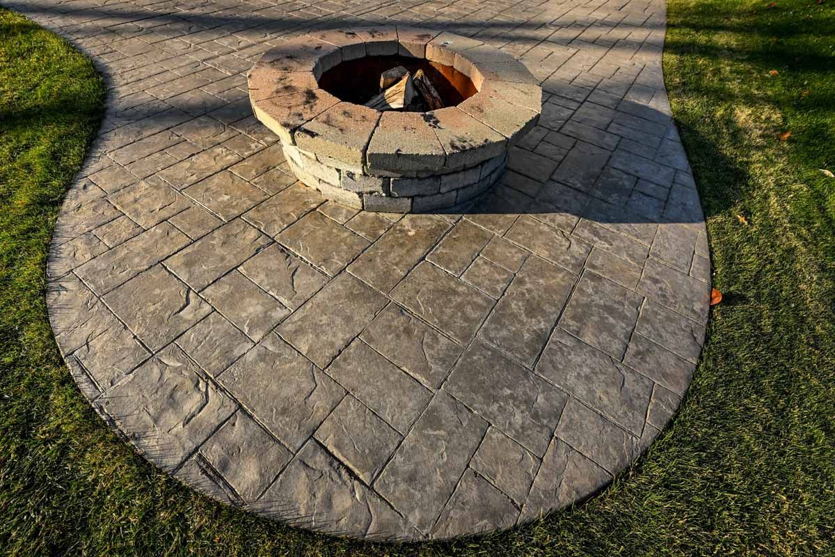 A circular fire pit surrounded by a stone paver patio set in a green grassy lawn.