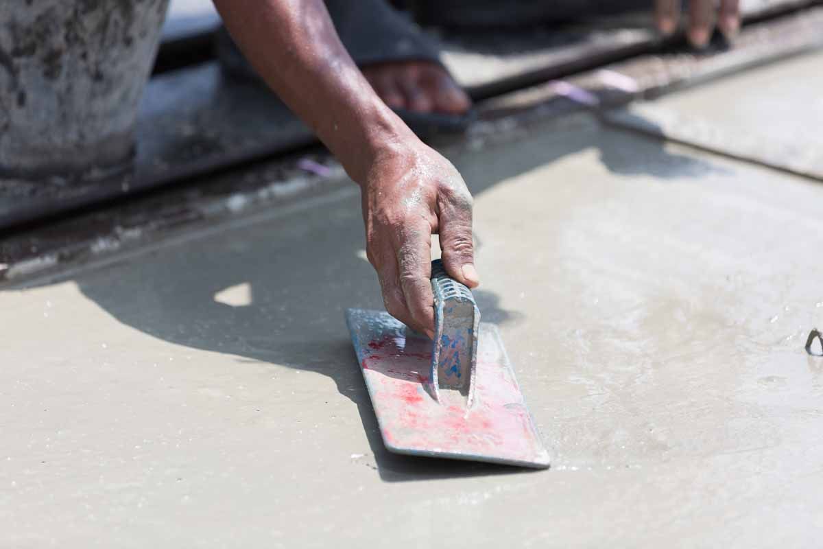 A worker uses a hand trowel to smooth wet concrete on a construction site.