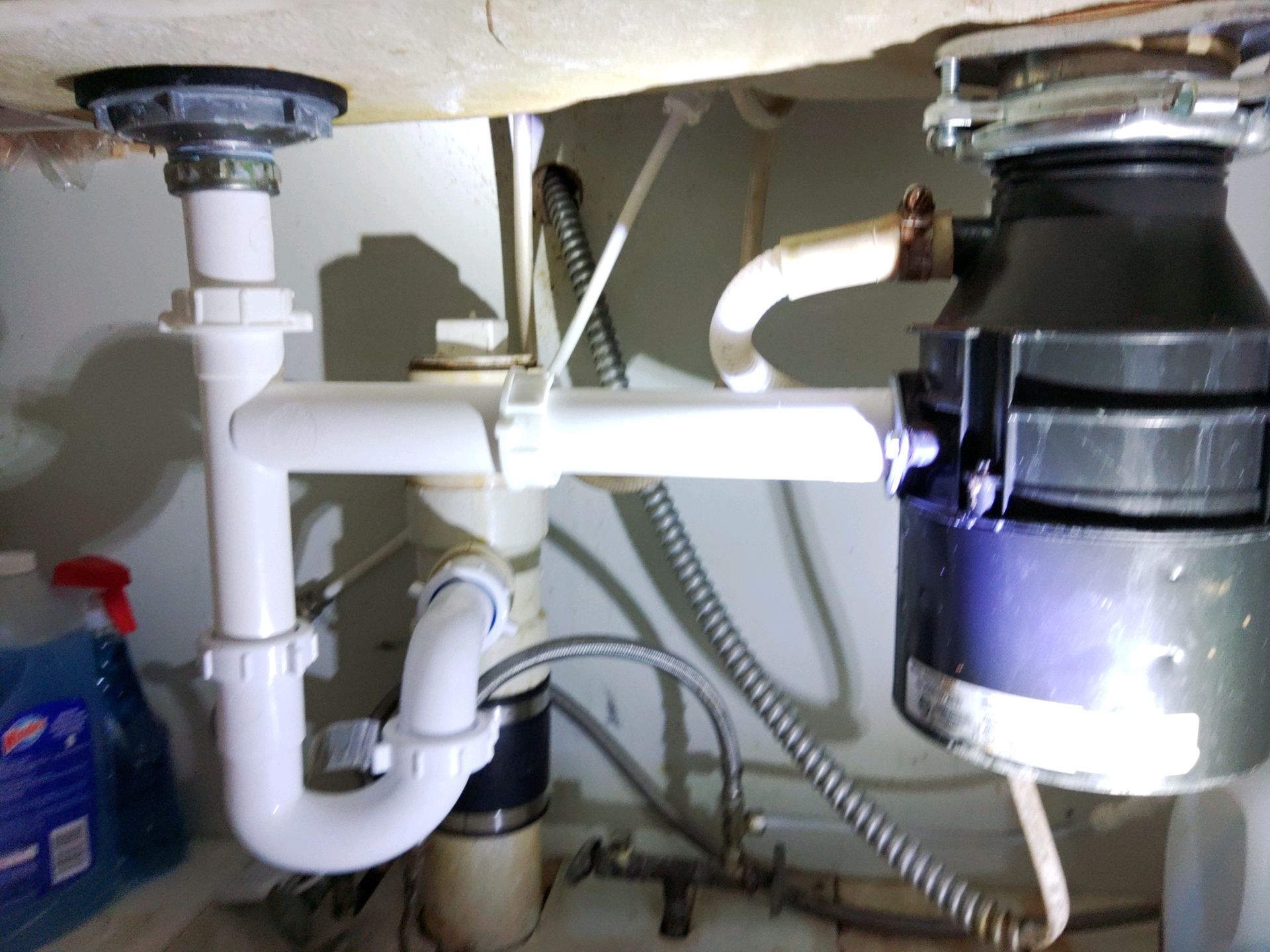The white PVC plumbing pipes and garbage disposal unit located under a kitchen sink.