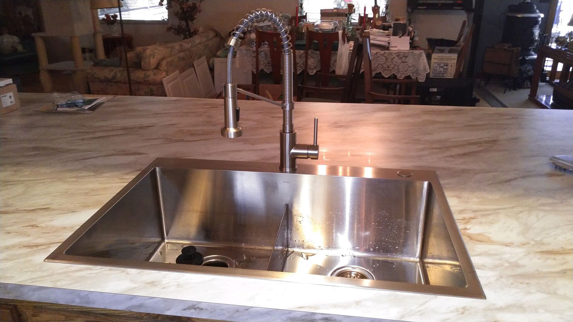 Stainless steel double-basin kitchen sink with a tall pull-down faucet set in a light-colored, marbled countertop.