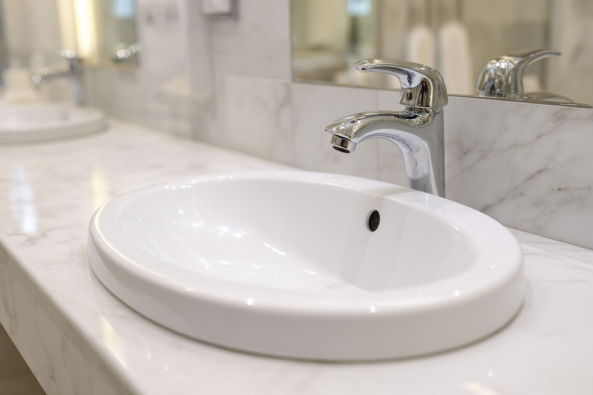 A white, oval bathroom sink with a chrome faucet set into a white marble countertop.