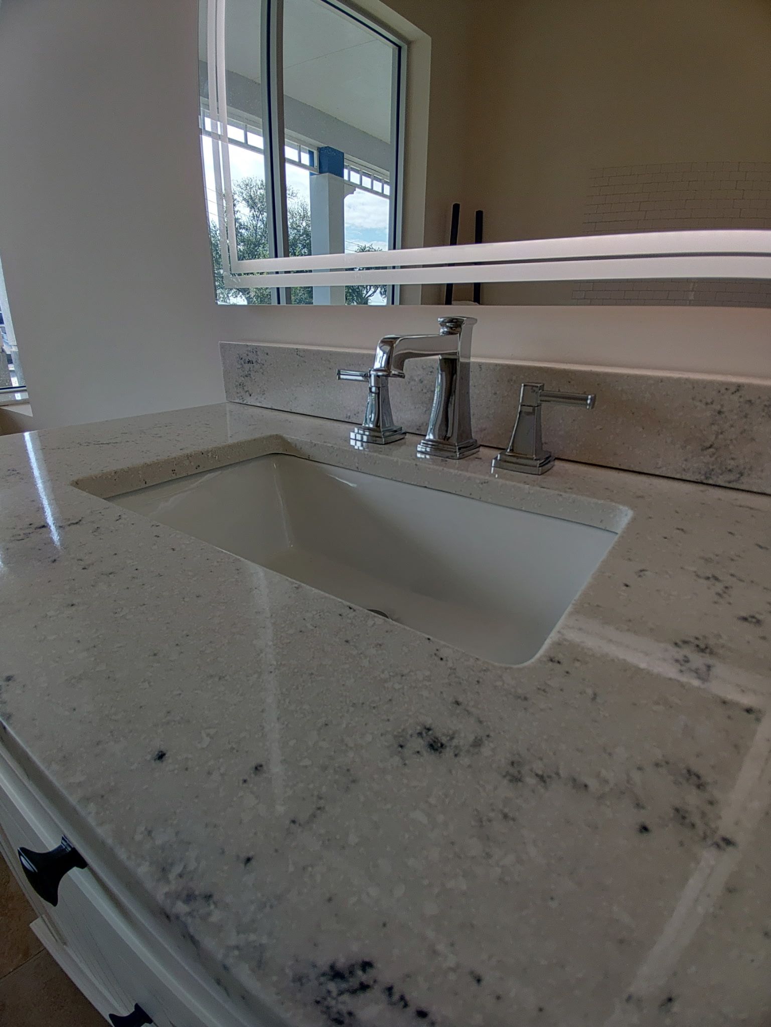 A white bathroom vanity with a speckled granite countertop, a rectangular under-mount sink, and a chrome faucet.