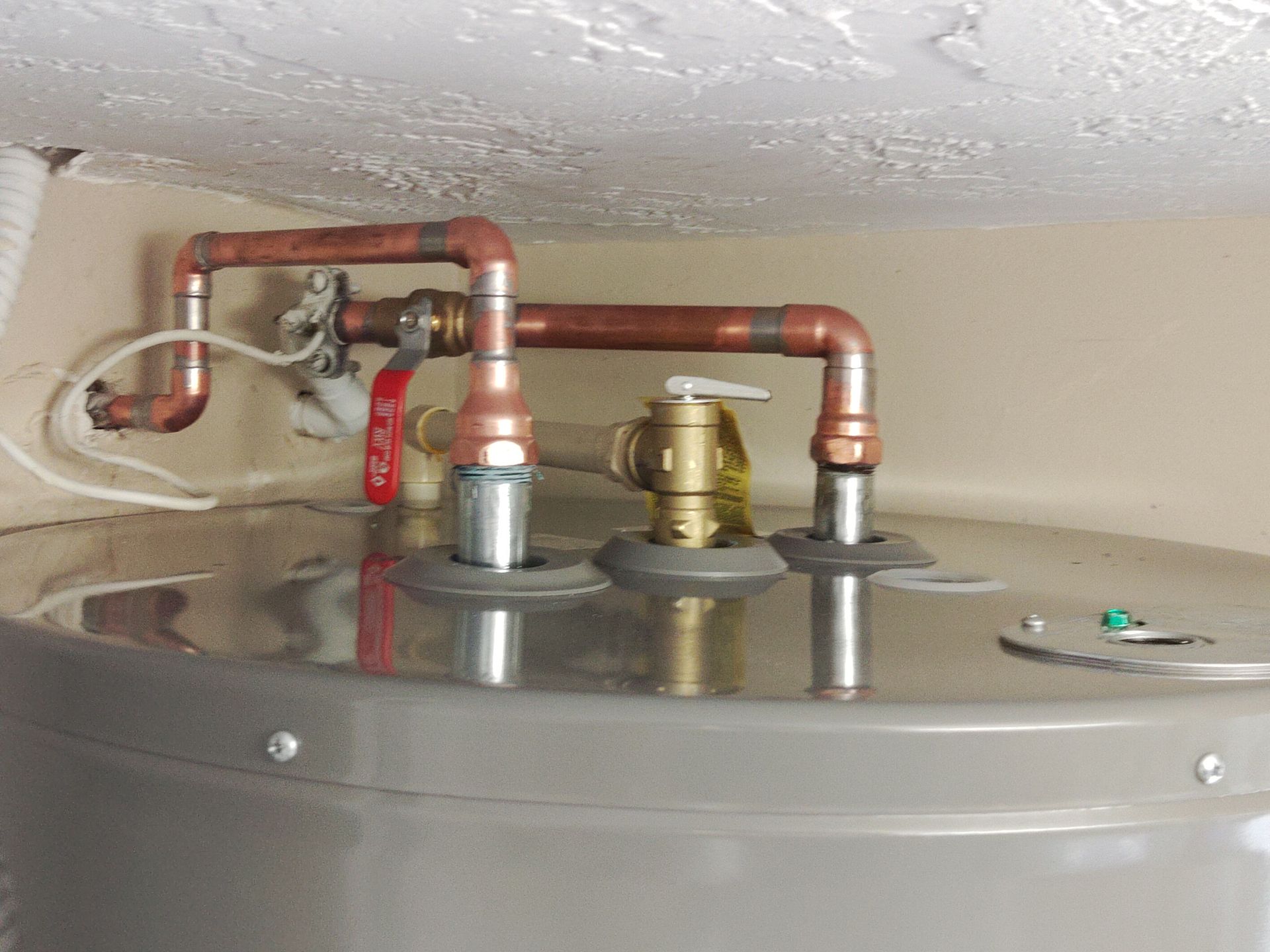 The top of a water heater showing copper pipes, a red shut-off valve, and a temperature pressure relief valve.