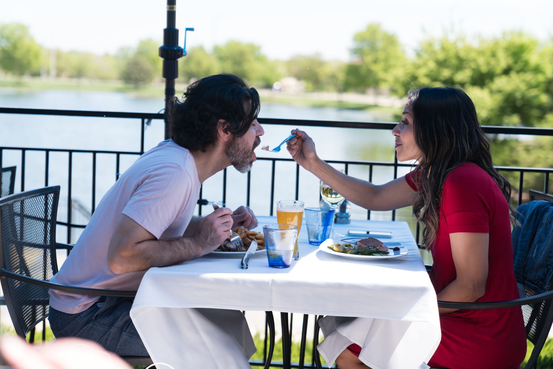 Couple at an outdoor dining spot, woman feeding man. 