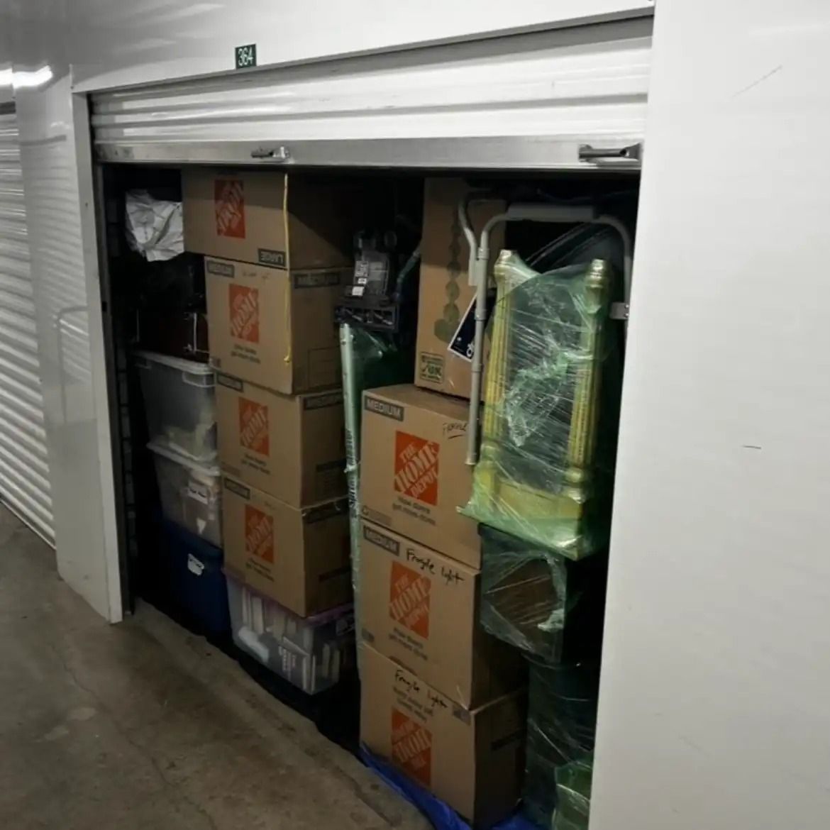 Storage closet packed with stacked cardboard boxes and wrapped items behind a partially open shutter.
