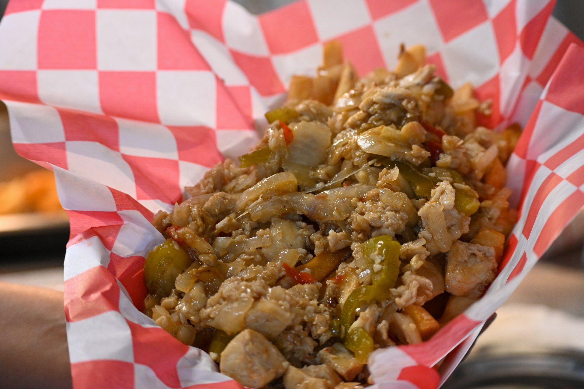A person is holding a basket of food in a red and white checkered paper.
