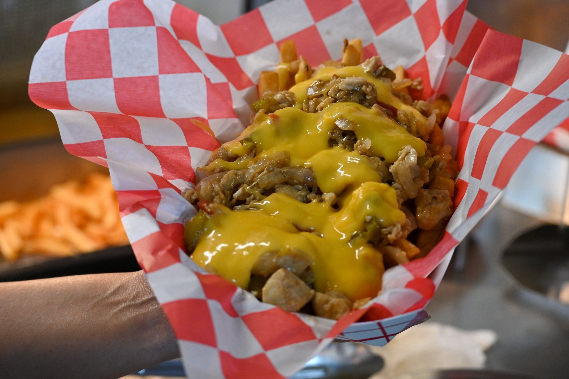 A person is holding a basket of french fries covered in cheese.