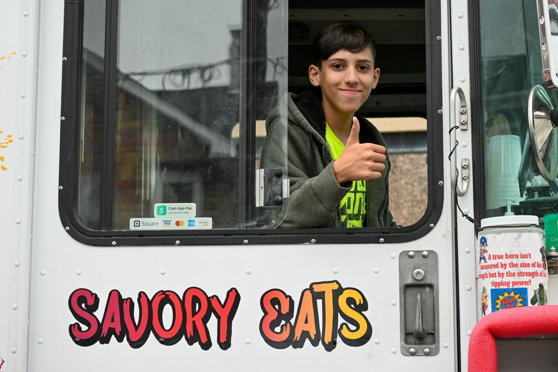 A young boy is giving a thumbs up from the window of a savory eats food truck.