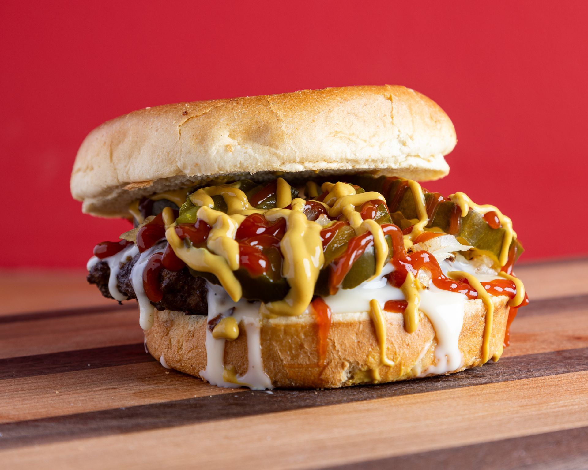 A close up of a hamburger with cheese , lettuce , tomatoes and bacon on a wooden table.