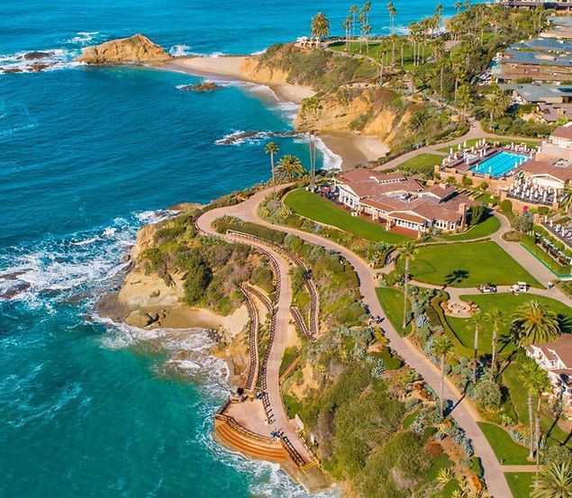 Aerial view of a coastal cliff resort with winding paths, turquoise water, and rocky shoreline