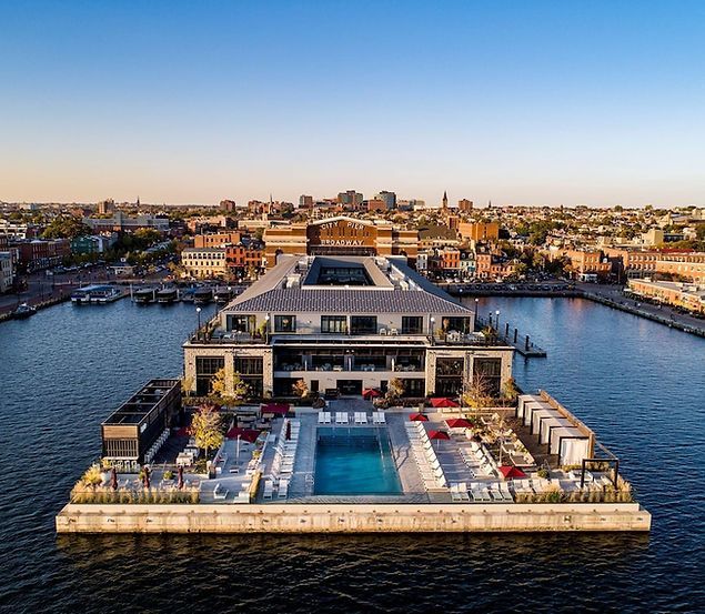 Aerial view of a waterfront luxury hotel with a central pool and cityscape in the background