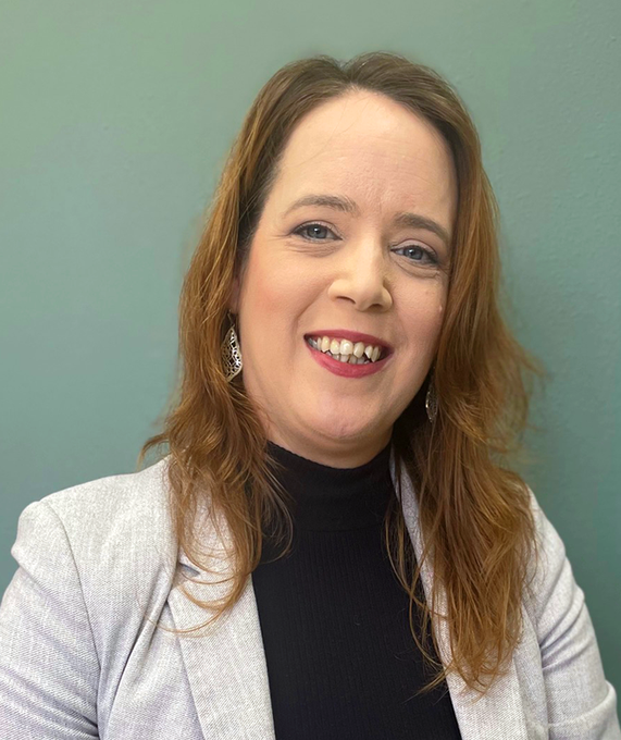 Woman in a light blazer smiles at the camera, against a teal background.