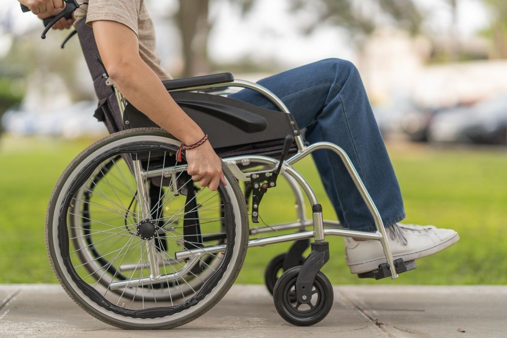 Person in a wheelchair on a sidewalk, hands on the wheel, blurred background.