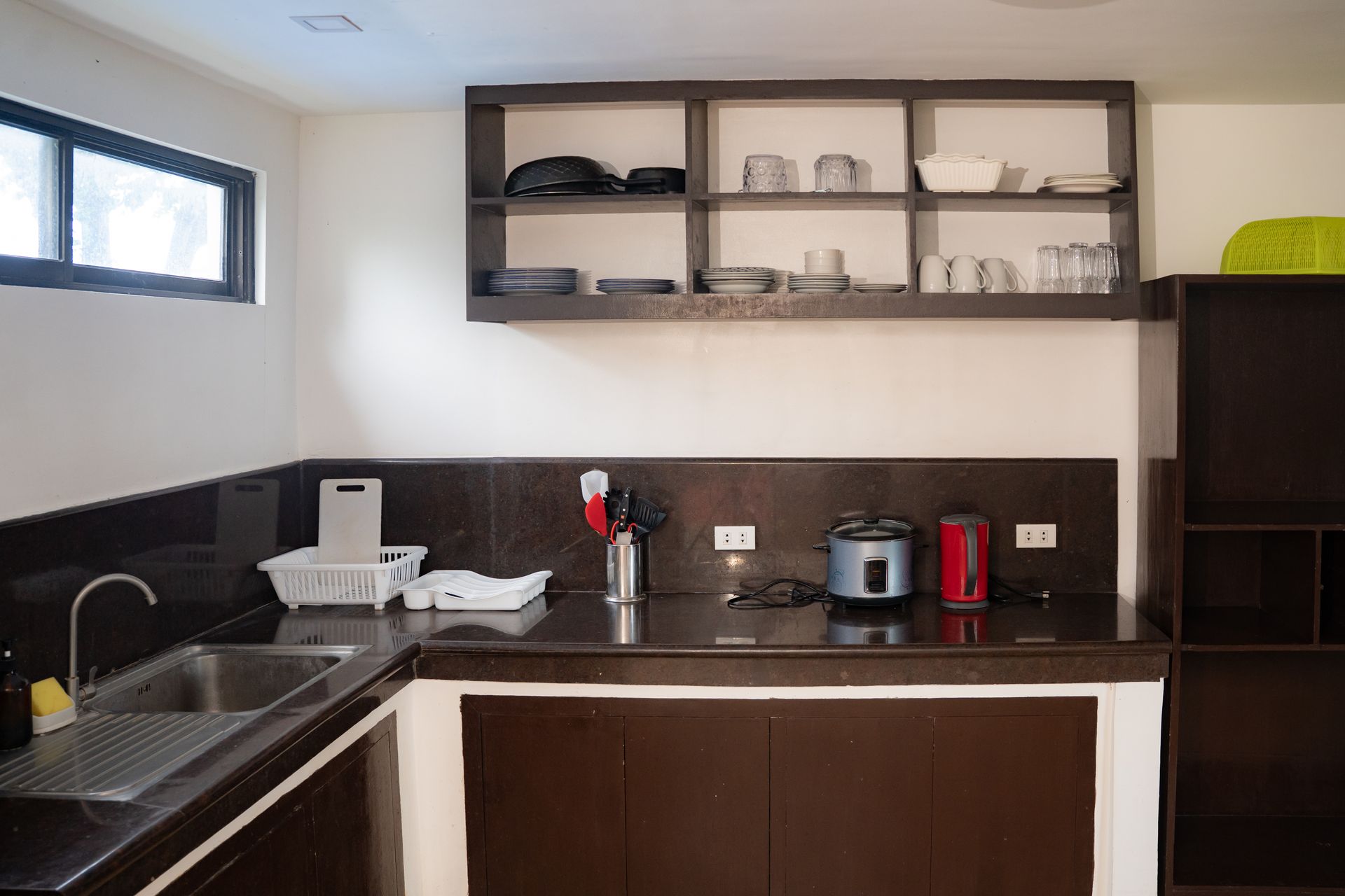 Kitchen with dark cabinets and countertops, a sink, and open shelving holding dishes and glasses.