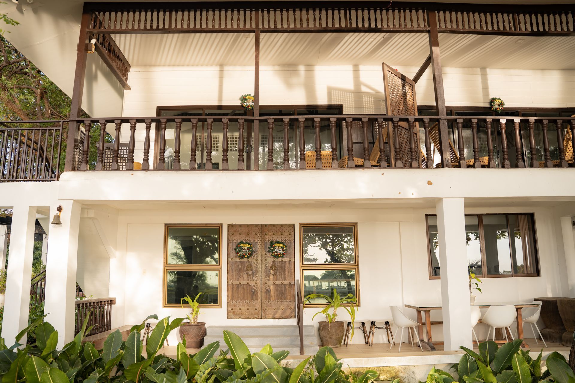 Two-story white building with wooden balconies, plants, and large windows.