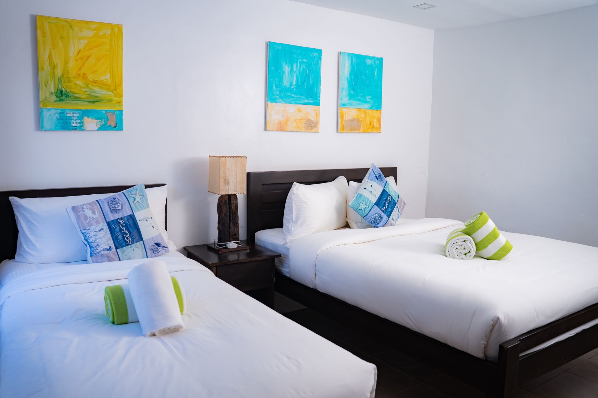 Bedroom with two beds, white linens, colorful artwork, lamp on nightstand.