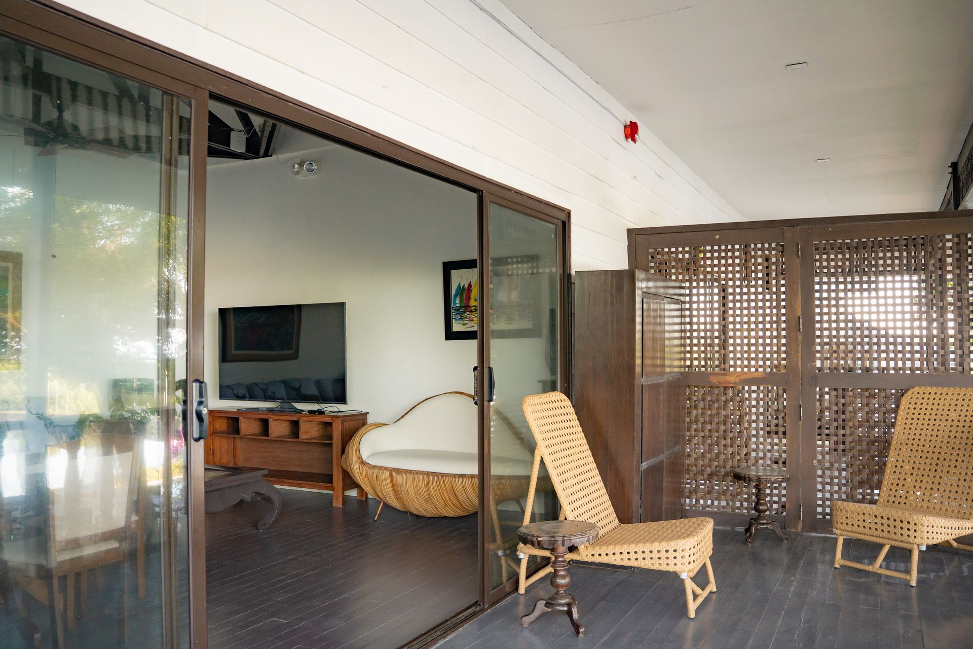 Open sliding glass doors reveal a living room with a sofa and artwork; a wicker chair sits on a porch.