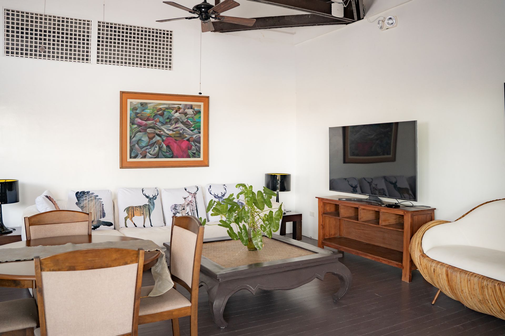Living room with a wooden cabinet, sofa, dining table, art, TV, and ceiling fan.