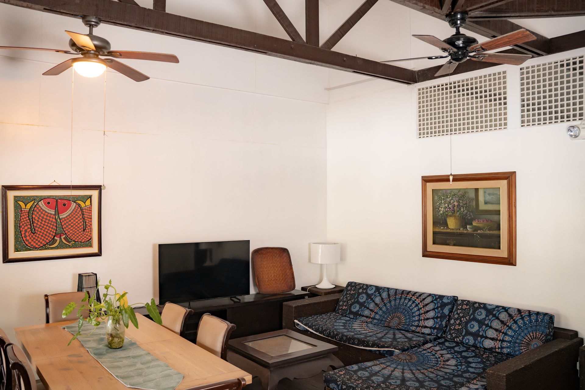 Living room with wood beams, fans, art, dark wood furniture, and a dining table.