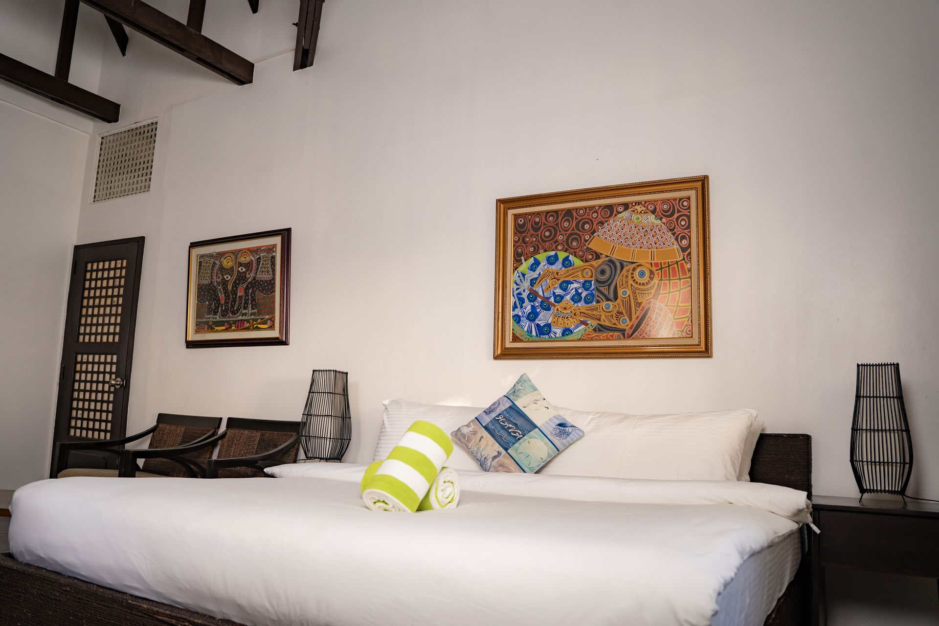 Bedroom with a large bed, art, and decor. White walls, wood accents, and a tropical style.