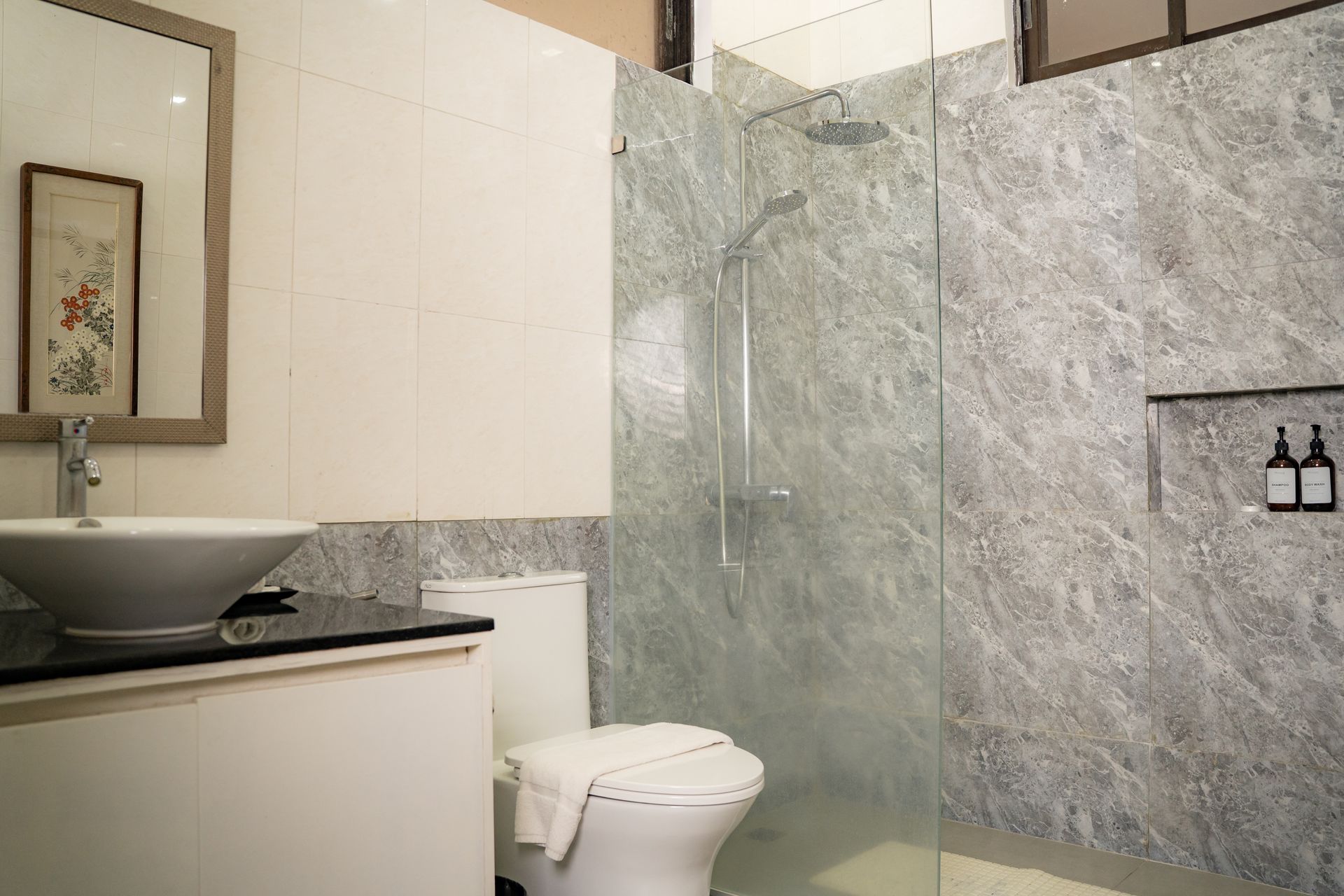 Bathroom with a marble-patterned shower, a toilet, a sink on a white cabinet, and a framed mirror.