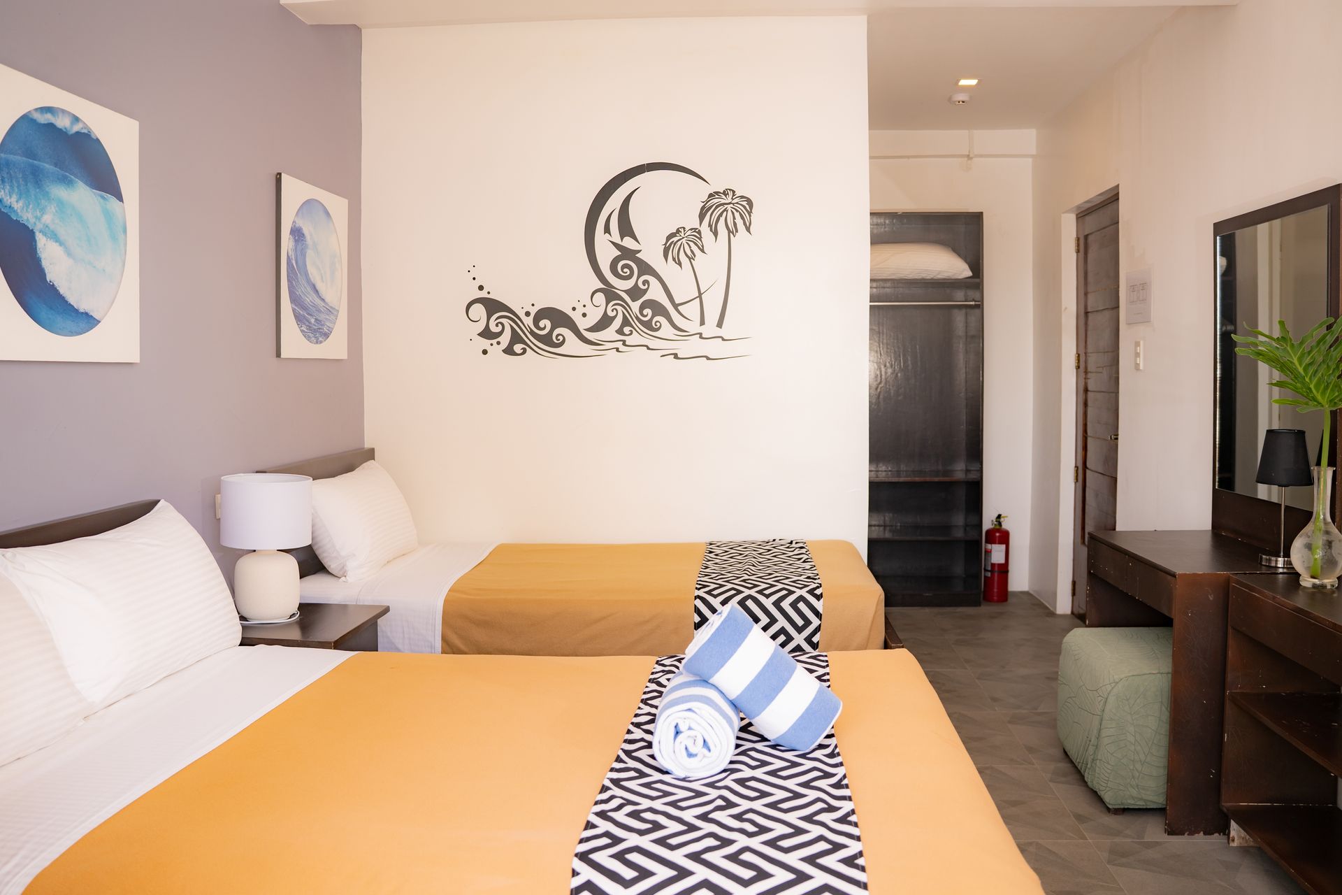 Hotel room with two beds, an orange bedspread, art, and a vanity.