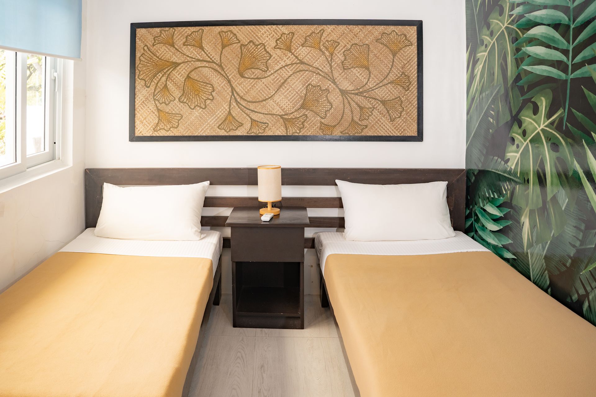 Two beds in a room with a nightstand. Botanical art on the wall, wallpaper with leaves.