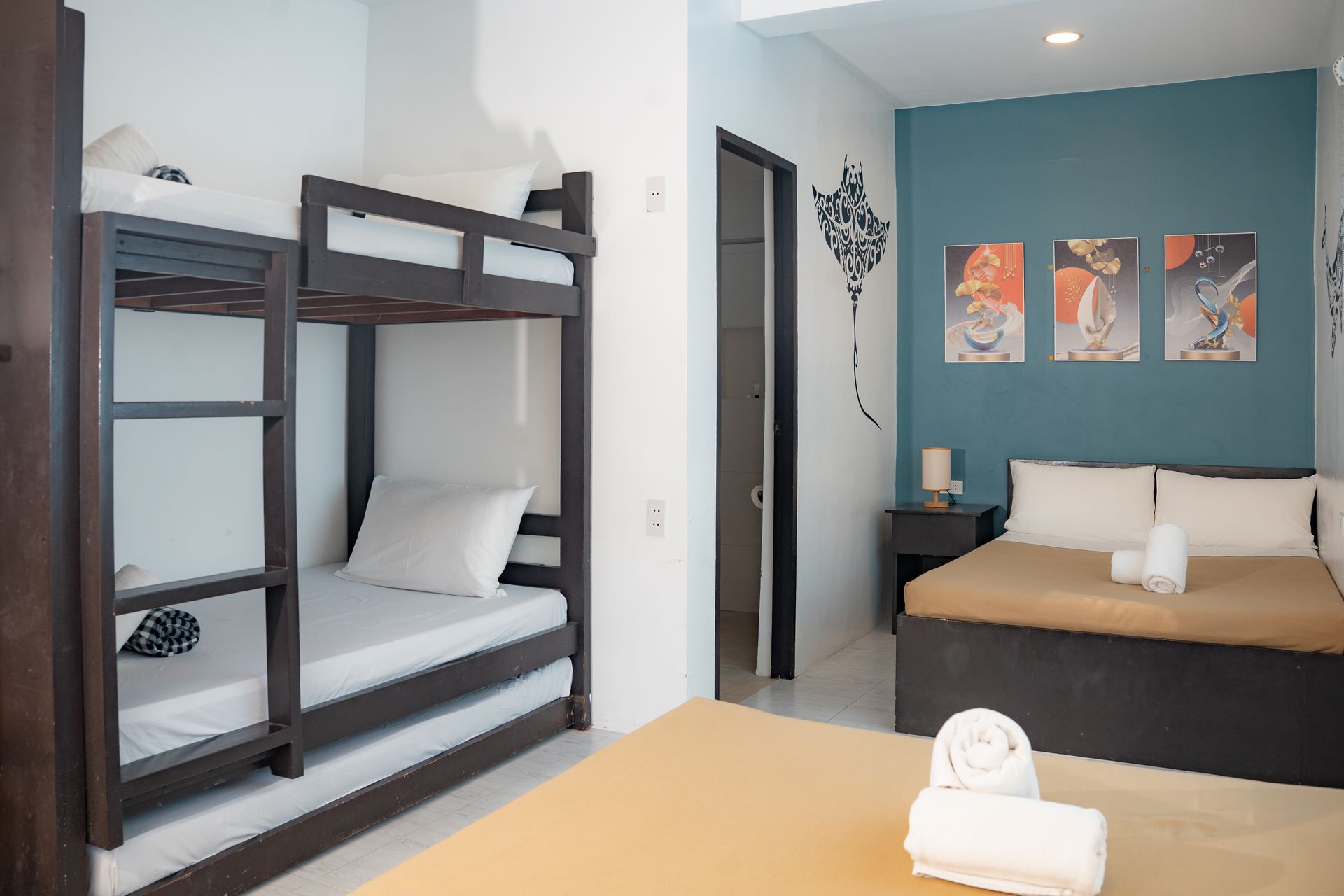 A room with bunk beds and a bed, blue accent wall with art, and an open doorway.